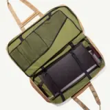 An open, green travel bag with multiple compartments and a padded section for a laptop.