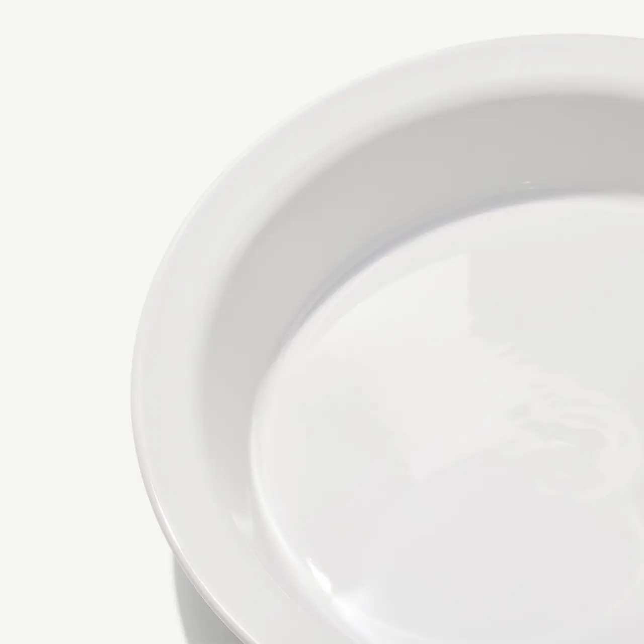 A close-up view of an empty white plate on a light background.