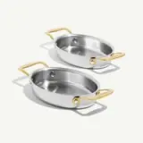 Two stainless steel cooking pans with gold-colored handles are placed side by side, casting soft shadows on a light background.