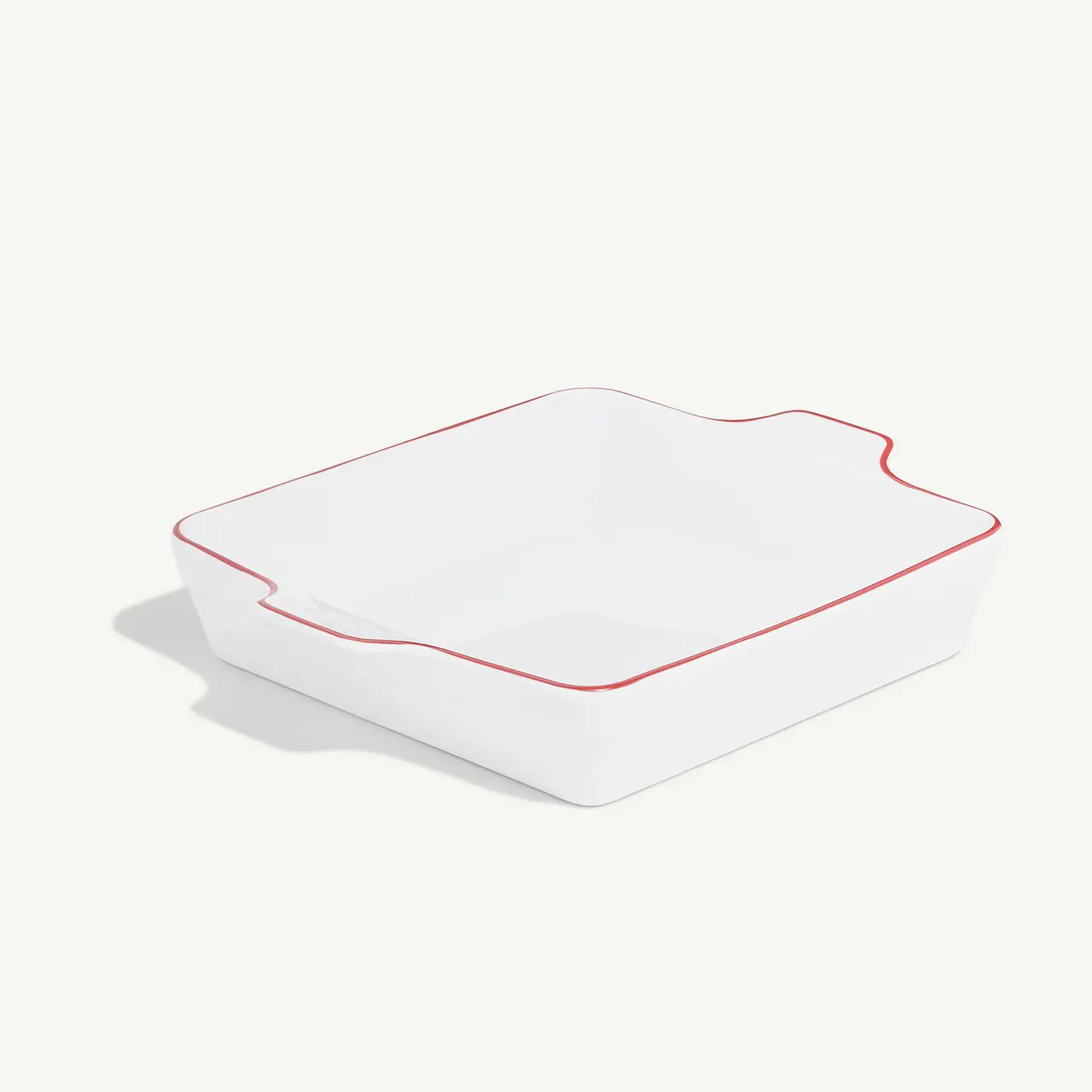 A simple white square ceramic dish with a wavy edge and a red trim stands against a plain background.