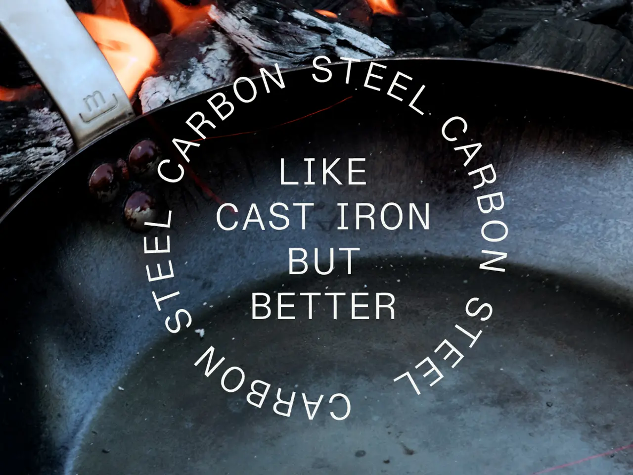 A carbon steel pan with the words "CARBON STEEL LIKE CAST IRON BUT BETTER" etched inside sits over an open flame, with a wooden handle at the edge.