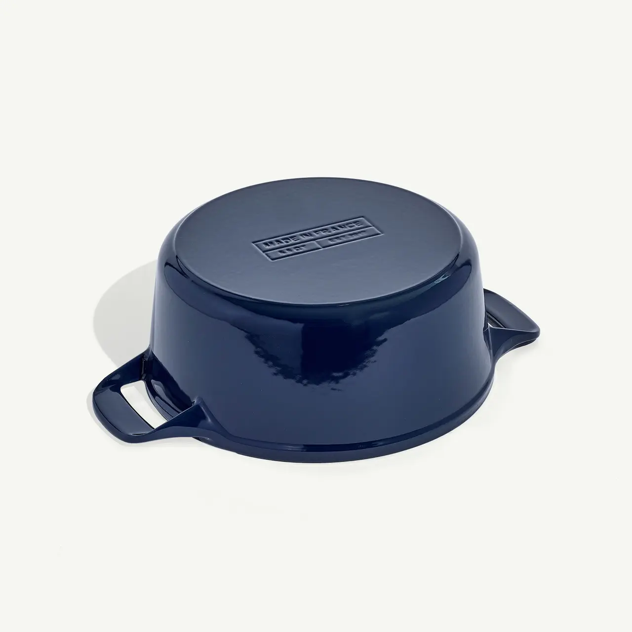 A dark blue, round casserole dish with lids and handles rests on a light background.