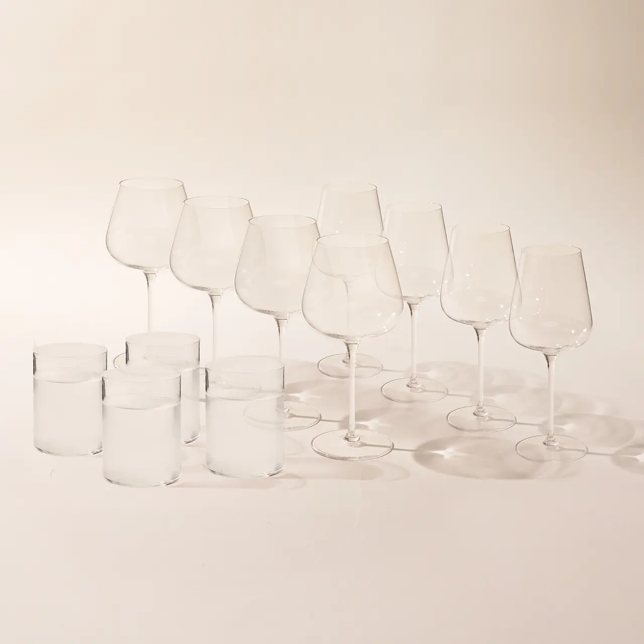 Several clear wine glasses and water glasses are arranged on a table with a neutral background.