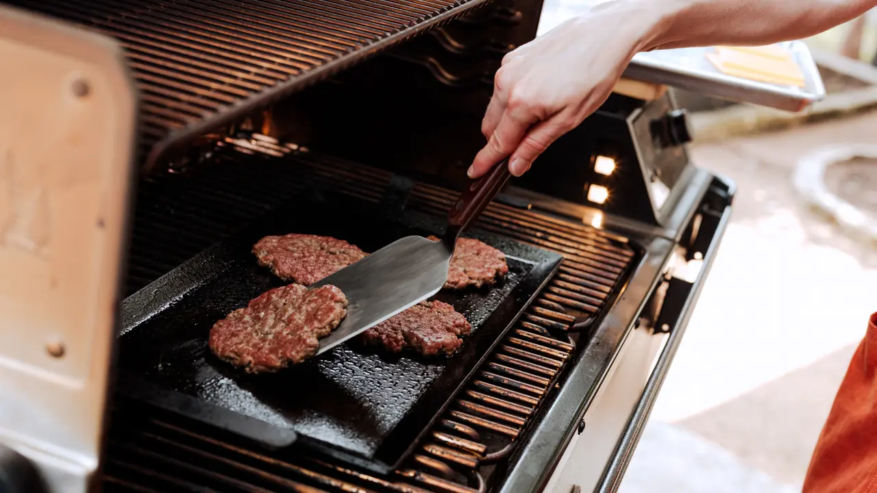 A person grills burgers on an outdoor barbecue grill using a spatula.