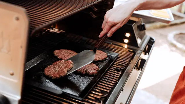 A person grills burgers on an outdoor barbecue grill using a spatula.