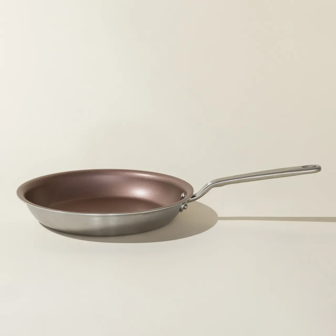 A stainless steel frying pan with a non-stick copper-colored interior and a long handle rests on a neutral background.