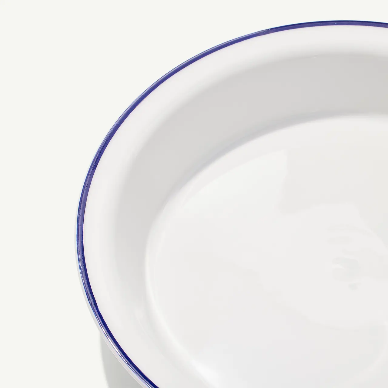 A close-up view of a plain white plate with a blue rim on a white background.
