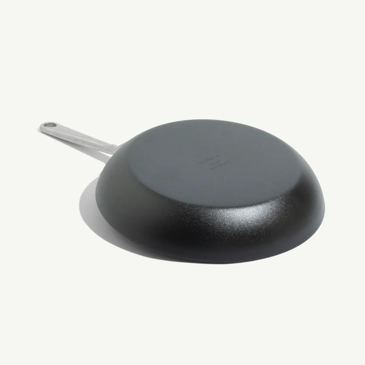 A black frying pan with a silver handle is shown against a light background.