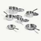 A collection of stainless steel cookware, including pots, pans, and lids, displayed on a light background.