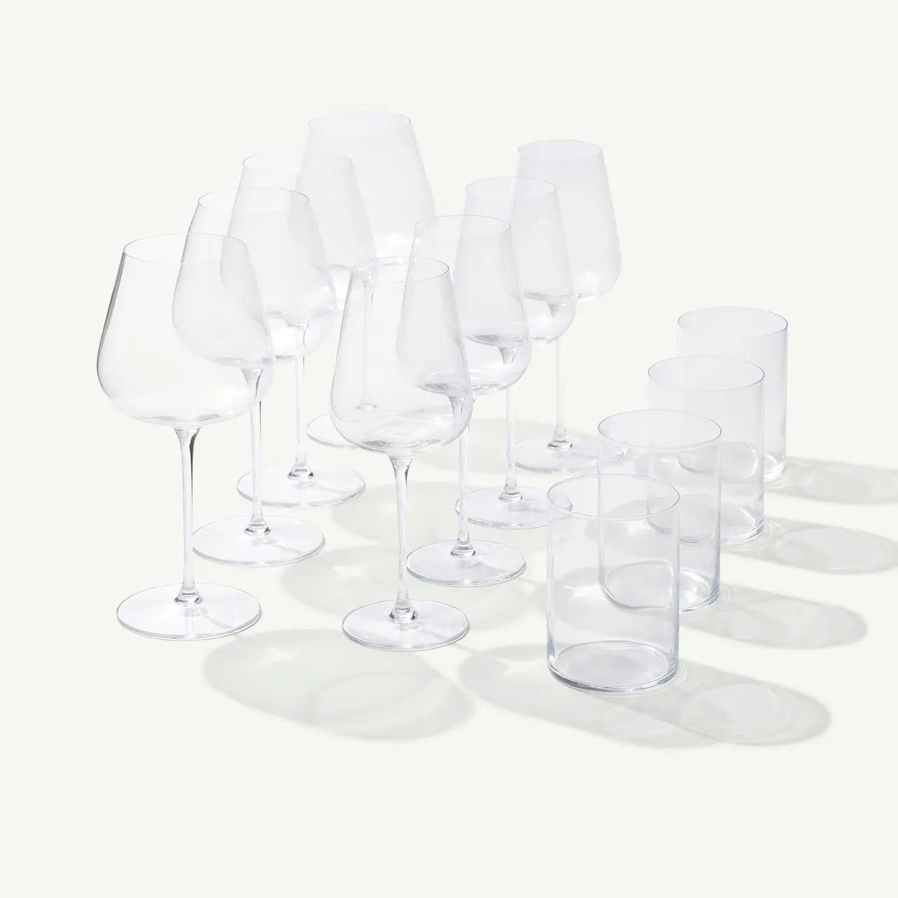 An assortment of empty wine and drinking glasses are neatly arranged on a surface, casting soft shadows under a bright light.