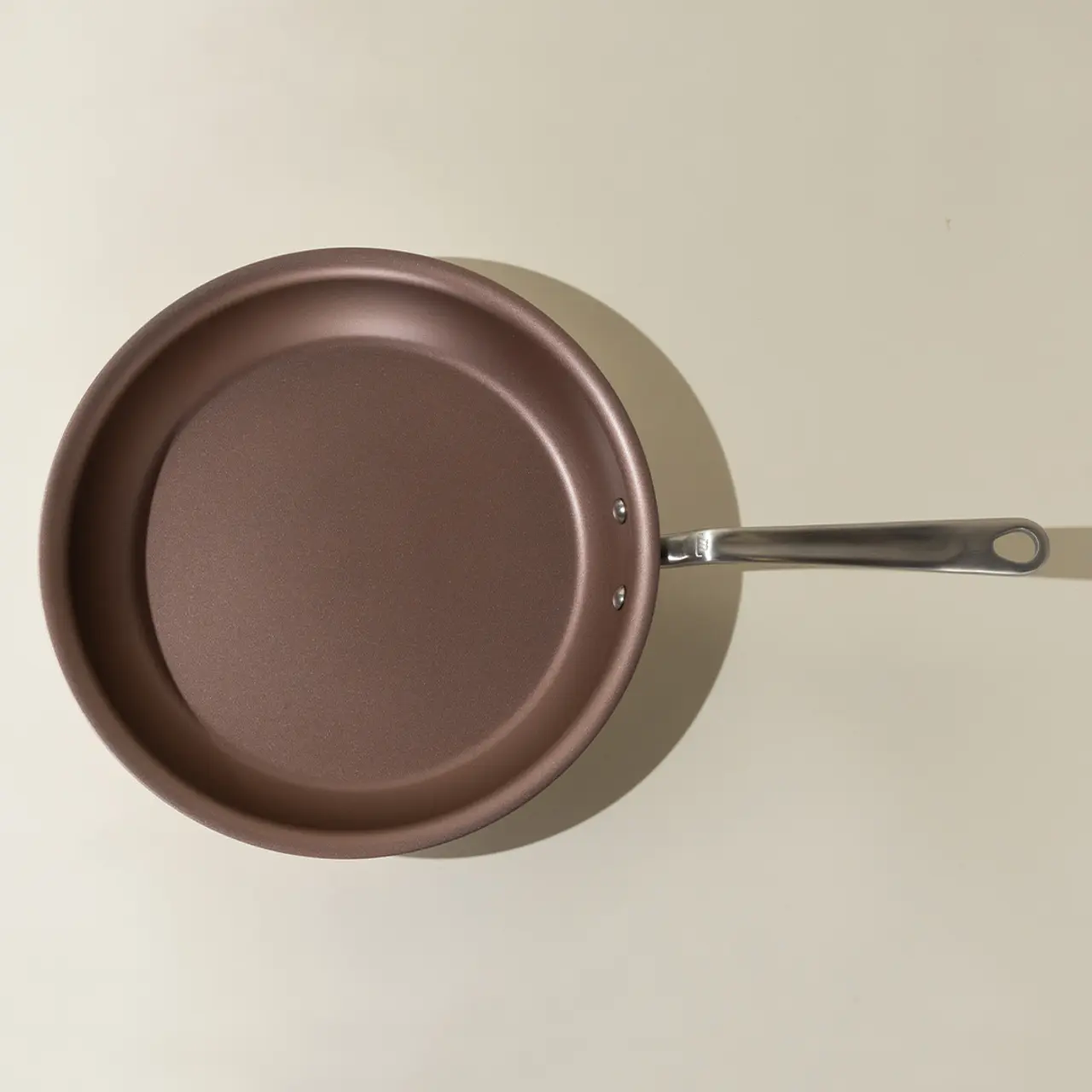 A brown non-stick frying pan with a silver handle is viewed from above against a neutral background.