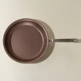 A brown non-stick frying pan with a silver handle is viewed from above against a neutral background.