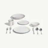 A set of white dishware, including plates, a bowl, a mug, and utensils with silver detailing.
