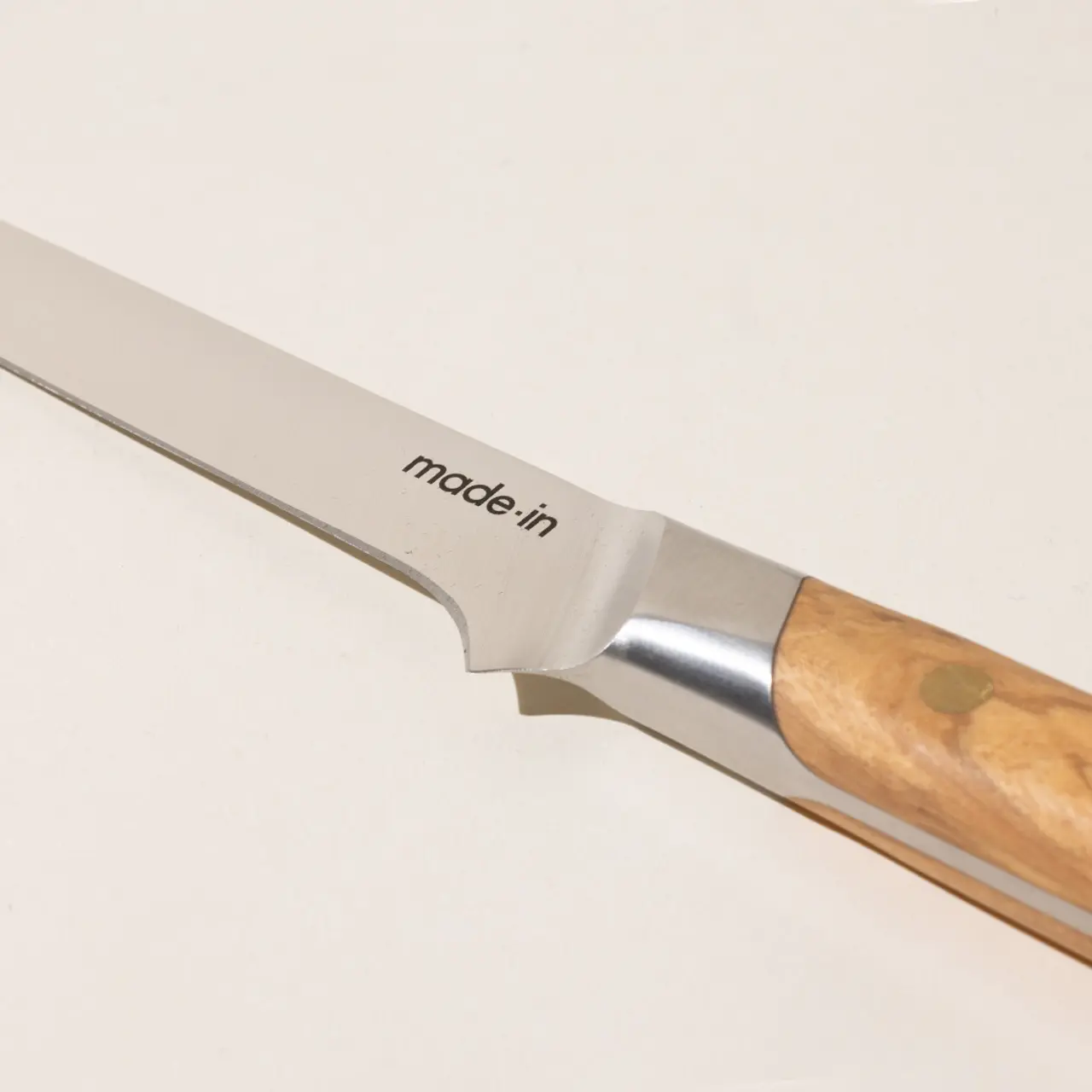 A close-up view of a kitchen knife with a wooden handle and the words "made-in" printed on the blade.
