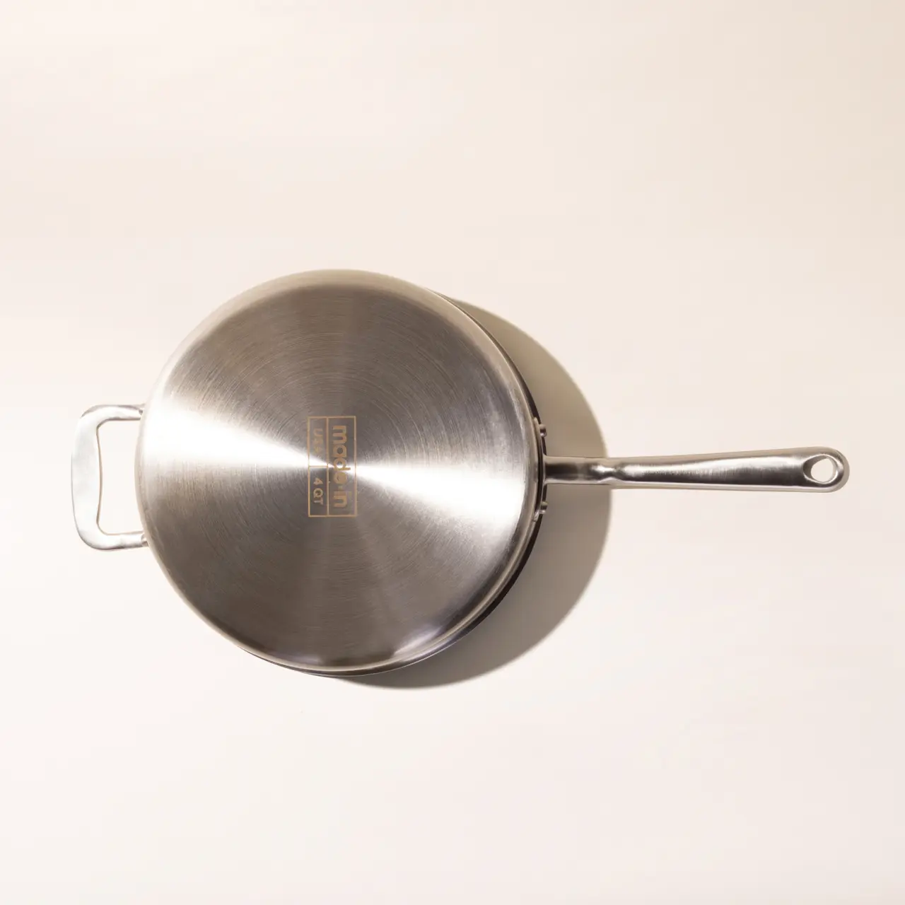 A stainless steel saucepan with a long handle positioned on a light surface.
