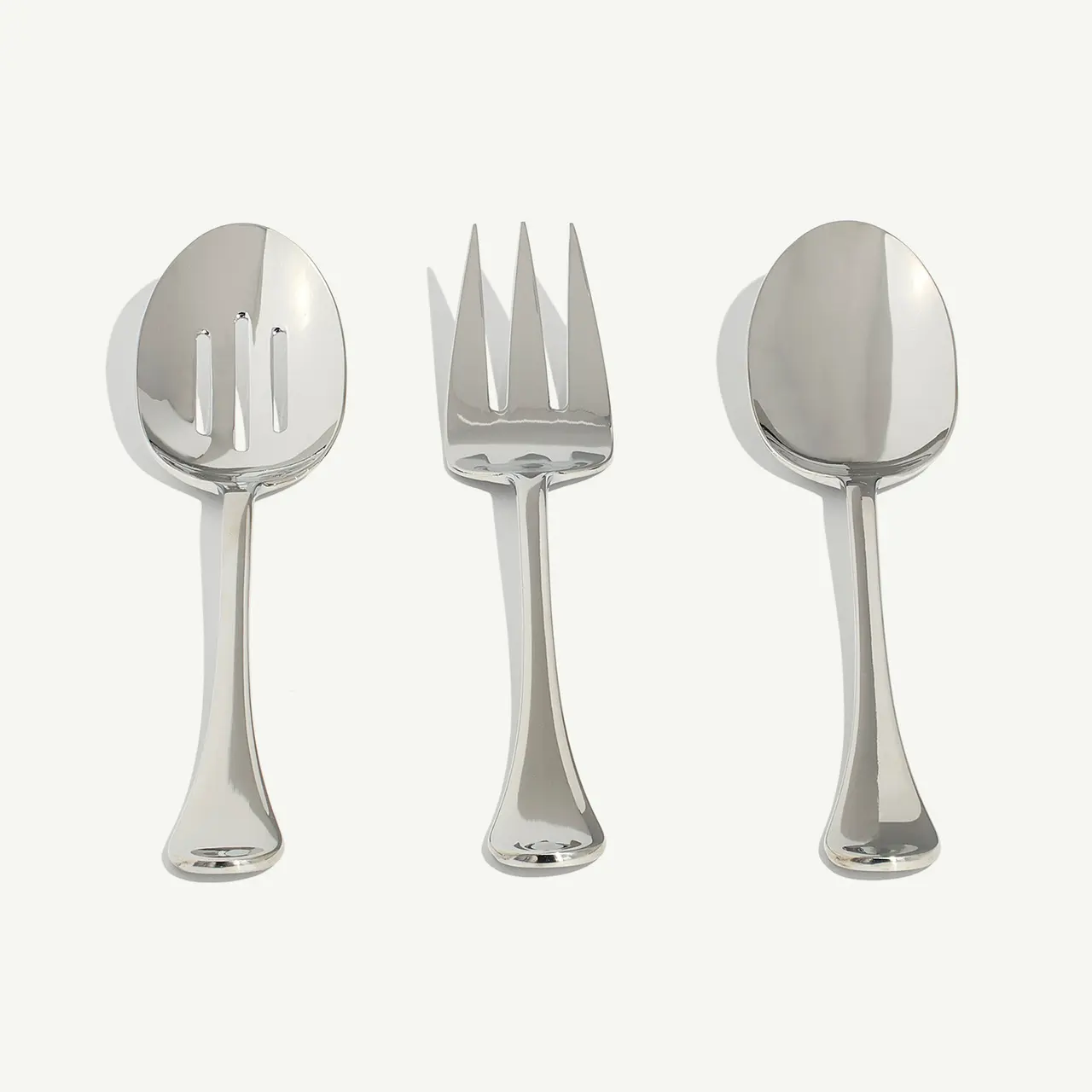 A slotted spoon, fork, and solid spoon are neatly arranged side by side on a plain background.