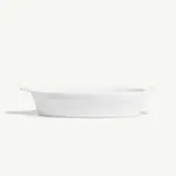 A simple white oval baking dish is displayed against a plain background.