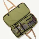 A green and tan carrying bag is open, revealing an organized set of barbecue tools, including a spatula, fork, and grill brush.