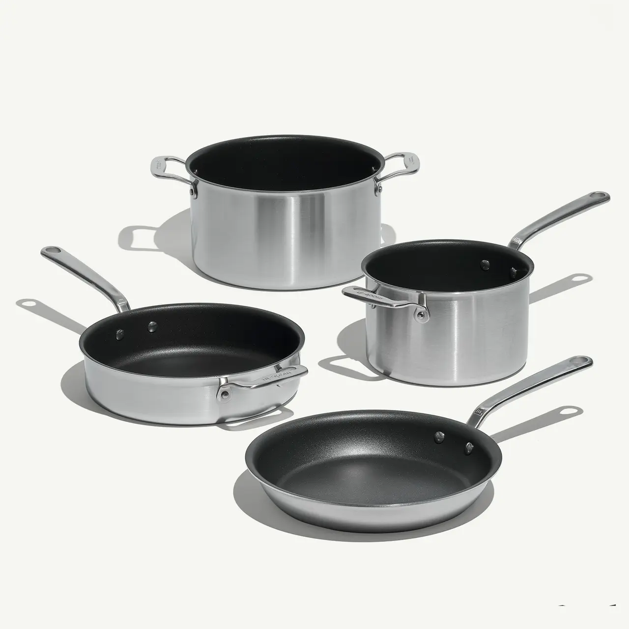 A set of stainless steel cookware, including two pots and two pans, is displayed on a white background.