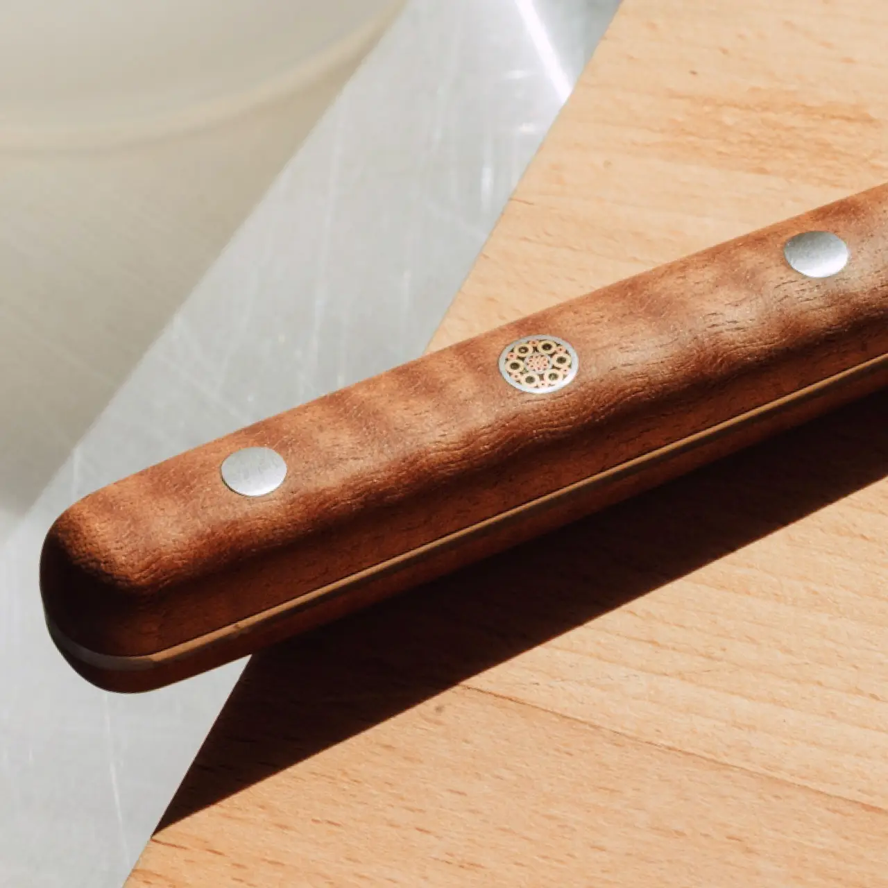 A wooden tool with metallic accents is placed on a wooden surface, bathed in natural light.
