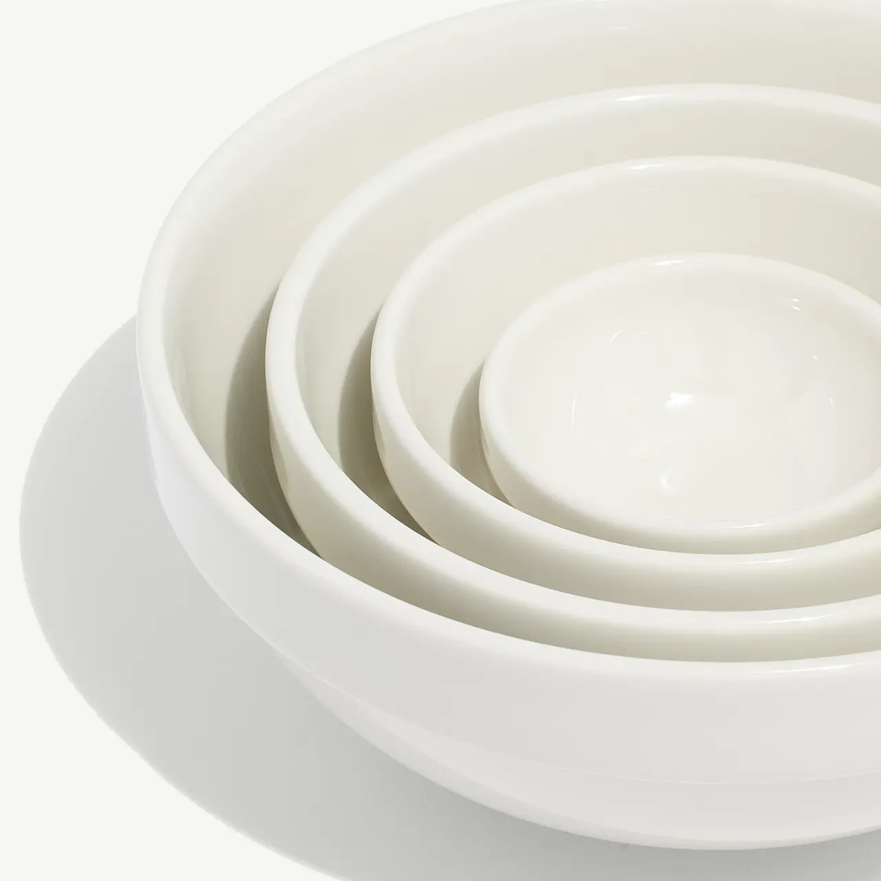A stack of clean, white nested bowls decreasing in size from large to small on a plain background.