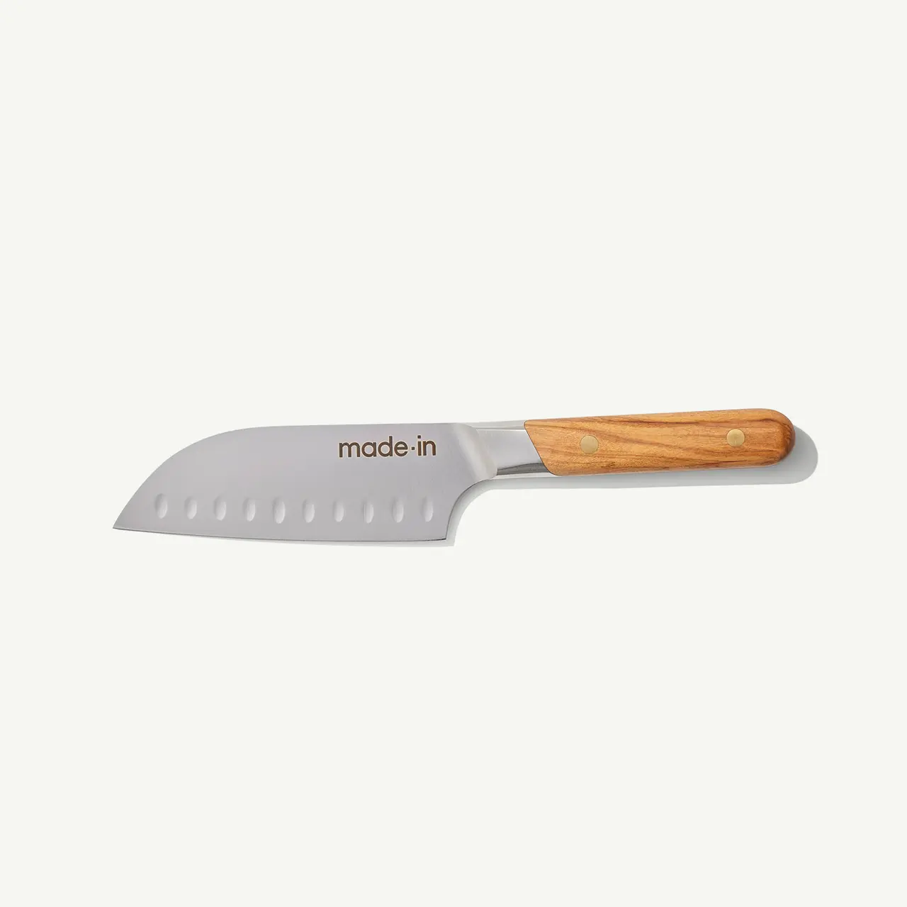 A stainless steel chef's knife with a wooden handle and perforated blade rests against a white background.