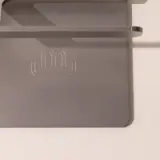 A close-up of a gray plastic object with a subtle "m" logo embossed on it, casting a soft shadow on a light surface.