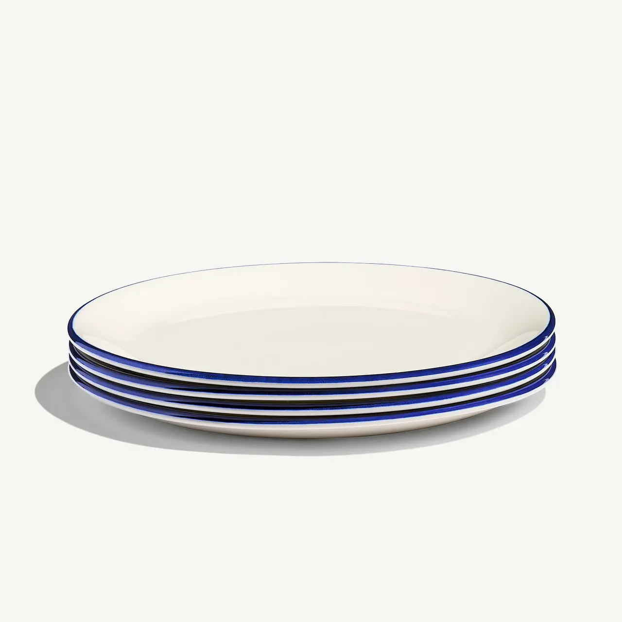 A stack of white plates with blue stripes on the rim sits against a neutral background.