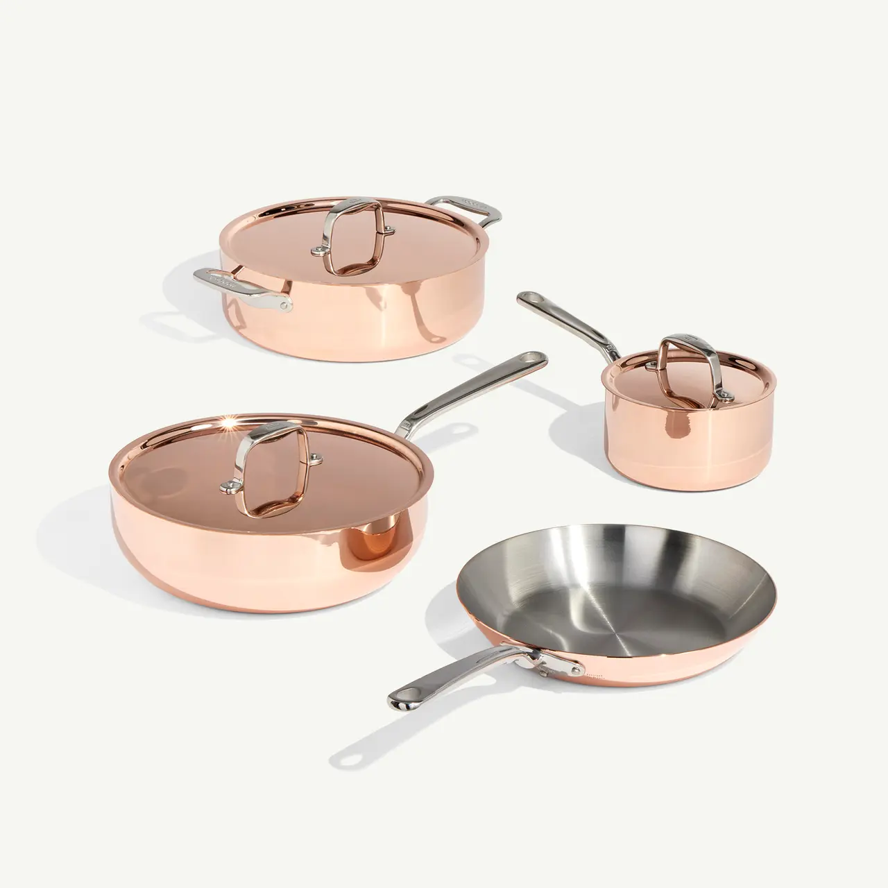 A set of copper cookware, including two pots with lids, a pan, and a saucepan, is neatly arranged on a light background.