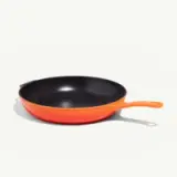 A black and orange frying pan is positioned on a light background.