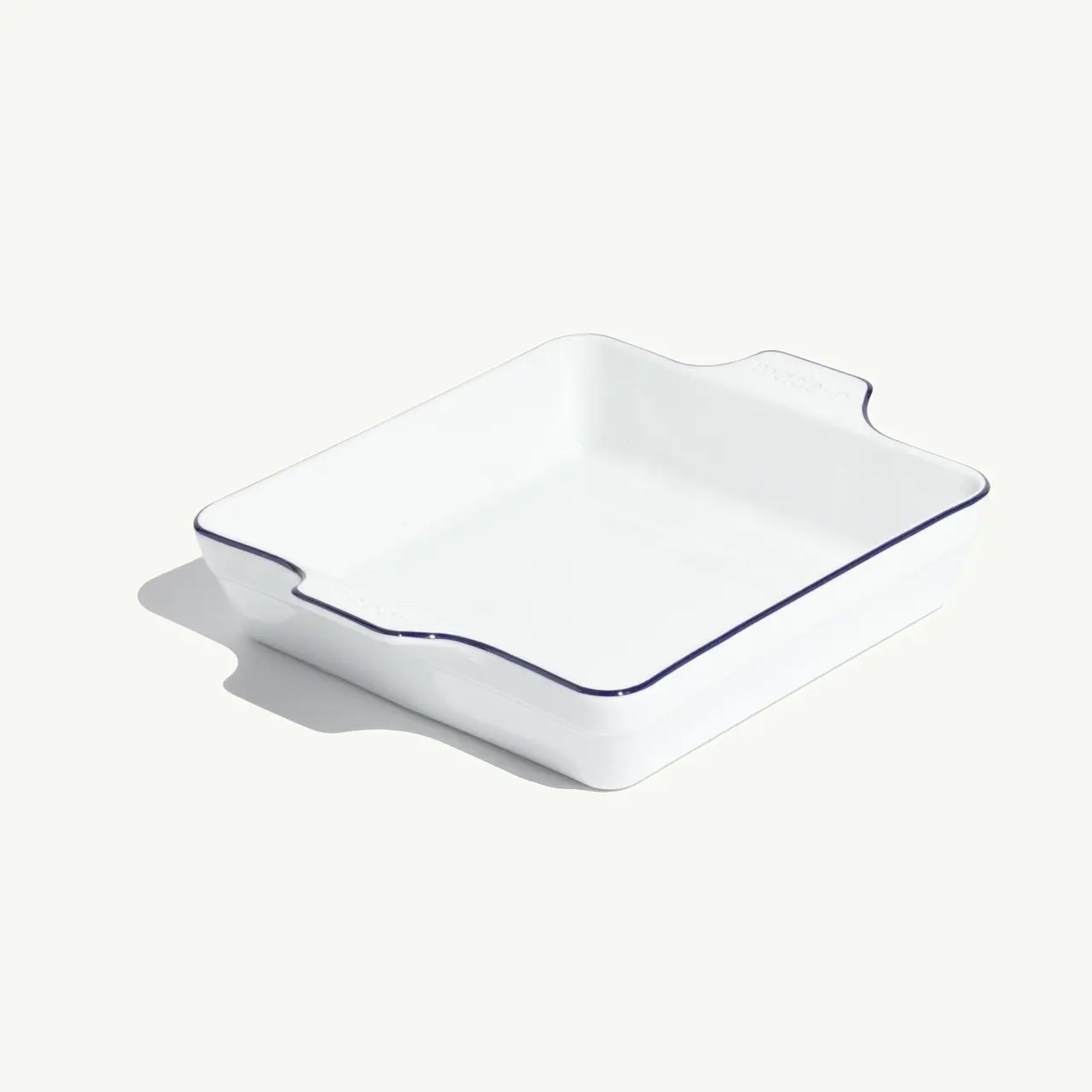 A white ceramic baking dish with blue trim sits on a light background, casting a soft shadow.