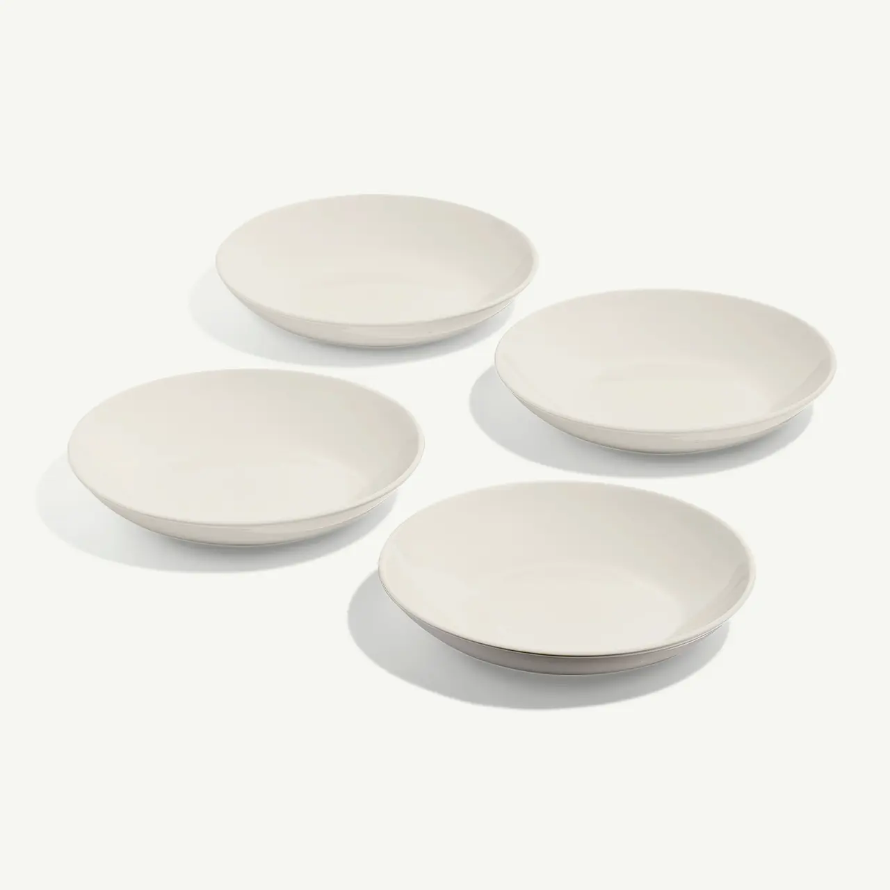 Four white, round, shallow bowls are arranged neatly on a light surface.