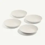 Four white, round, shallow bowls are arranged neatly on a light surface.