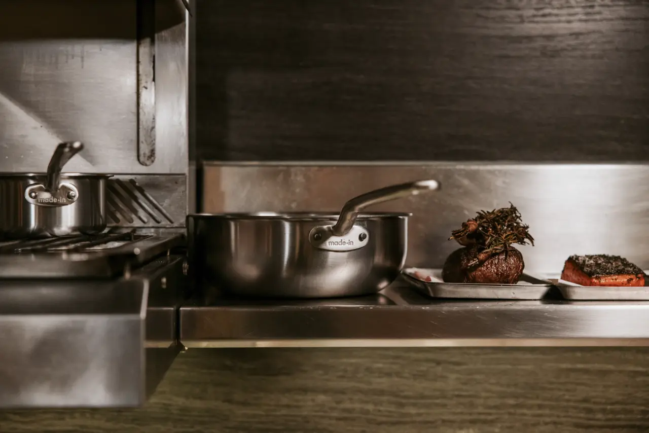 A stainless steel pot and a small dish with a roasted item sit on a countertop in a modern kitchen.