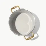 A stainless steel cooking pot with gold handles and a smooth interior surface is shown from a top-down perspective.