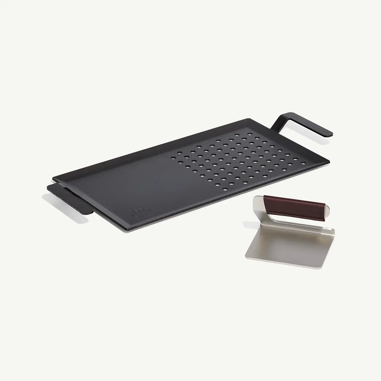 A black stove-top griddle with an attached handle and a small rectangular drip tray set on a light background.