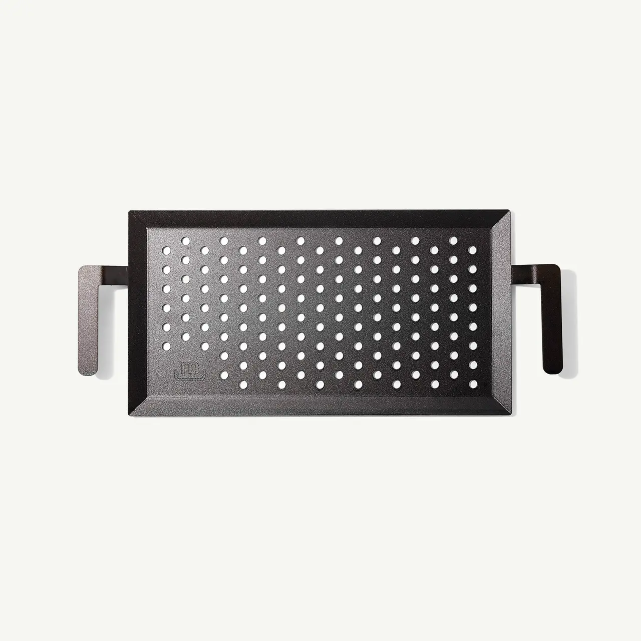 A rectangular, black grill pan with perforations and side handles set against a light background.