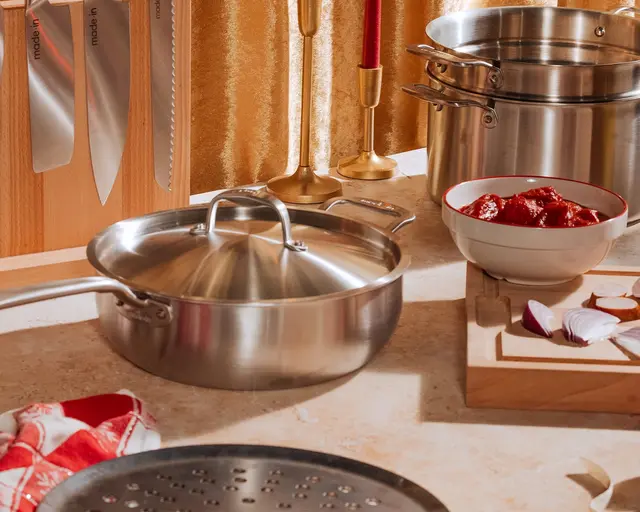 A variety of stainless steel cookware and red kitchen gloves on a countertop, indicating preparation for cooking.