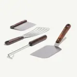 A set of four grilling tools featuring stainless steel heads and wooden handles, including a spatula, grill fork, and scraper.