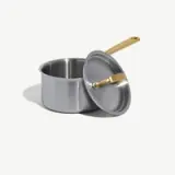 A stainless steel pot with a gold-colored handle rests beside its matching lid.