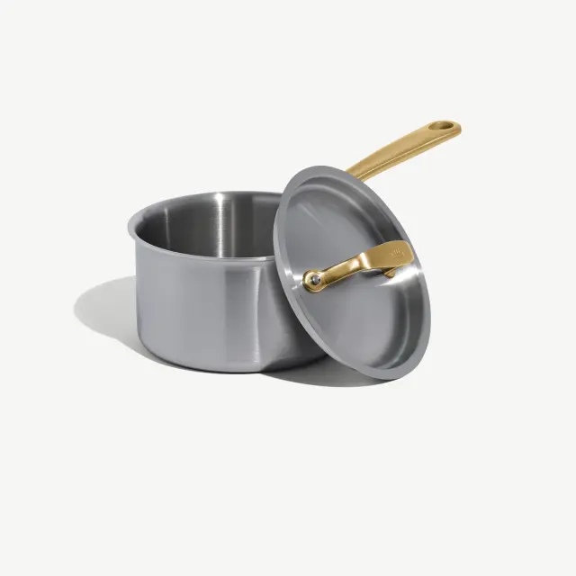 A stainless steel pot with a gold-colored handle rests beside its matching lid.