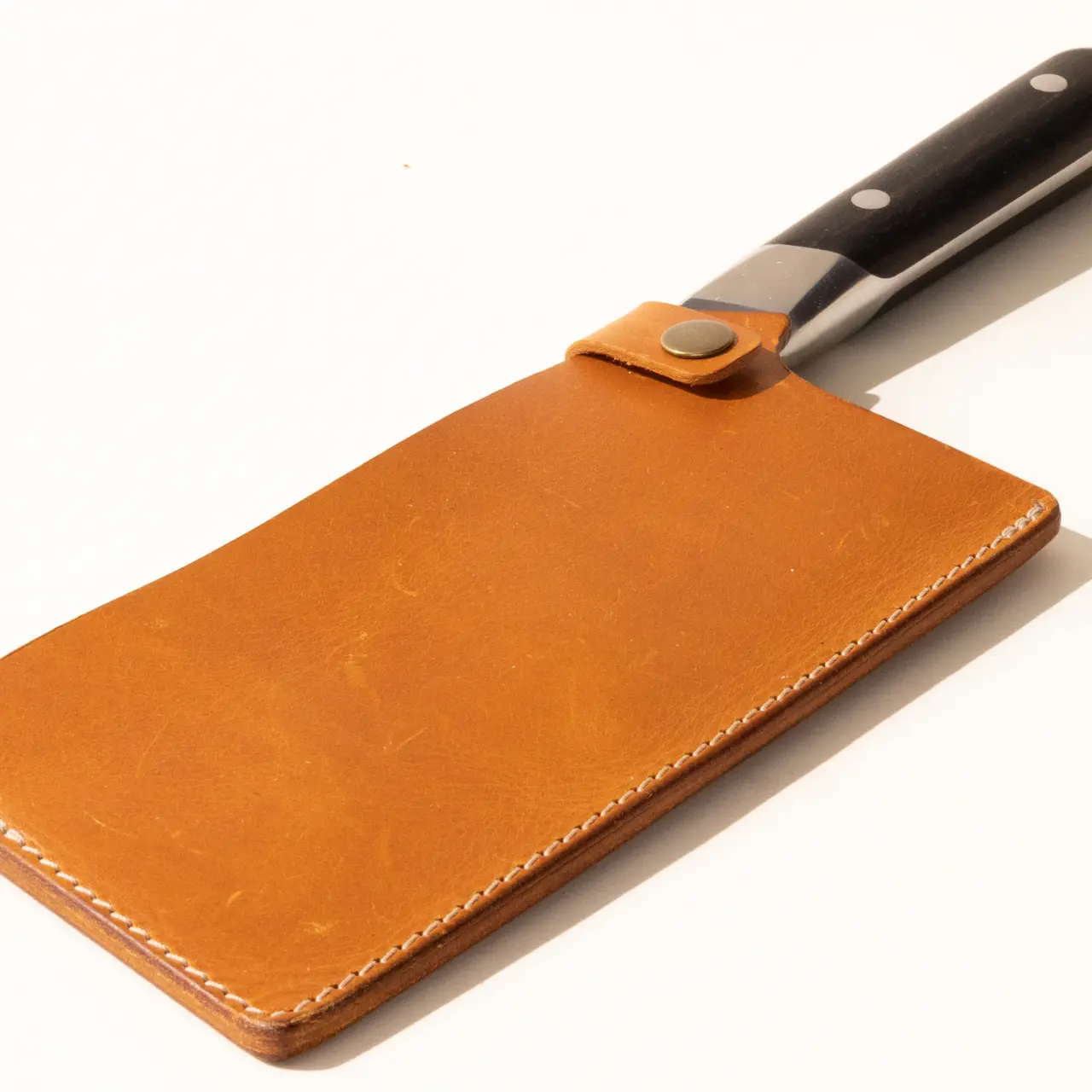 A kitchen knife with a black handle secured in a brown leather blade cover on a white background.