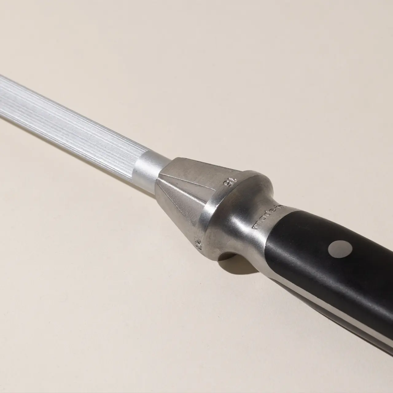 A close-up of a tuning fork positioned diagonally against a plain background showcases its metallic tines and black handle.