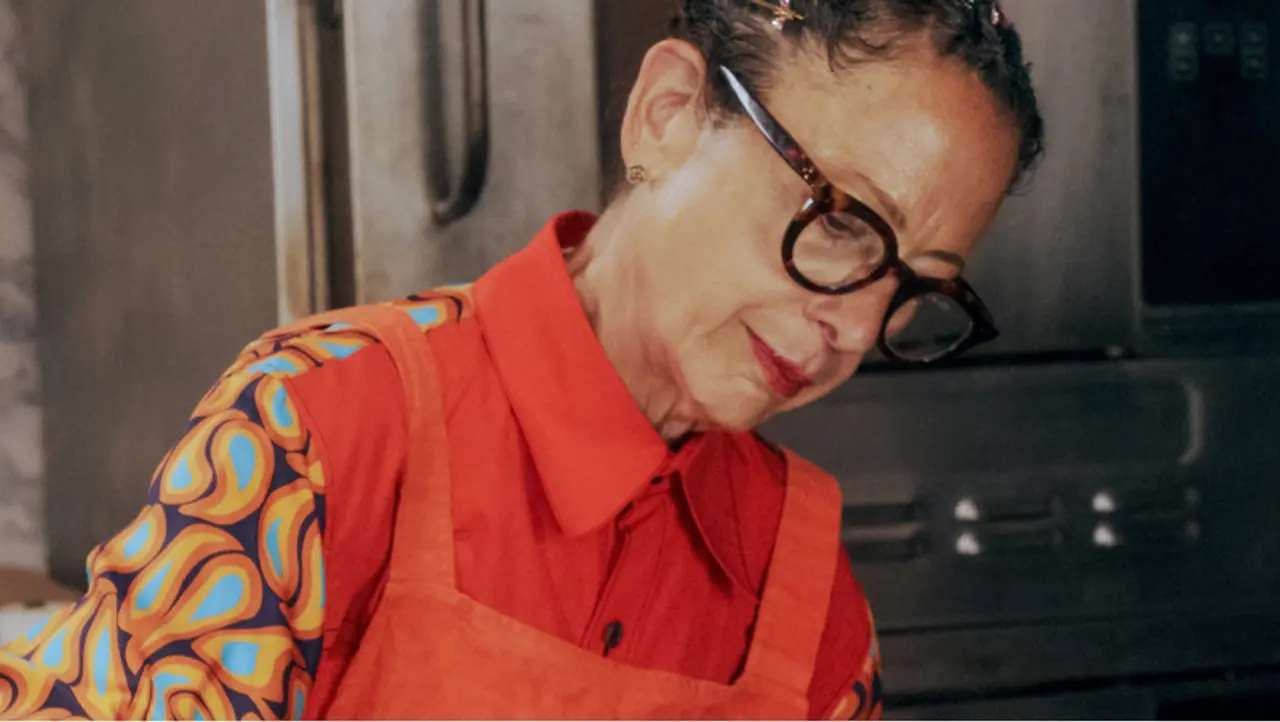 A person with glasses wearing a red top and a patterned apron is focused on a task in a kitchen setting.