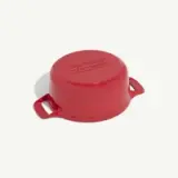 A red round casserole dish with handles is displayed upside down on a light background.