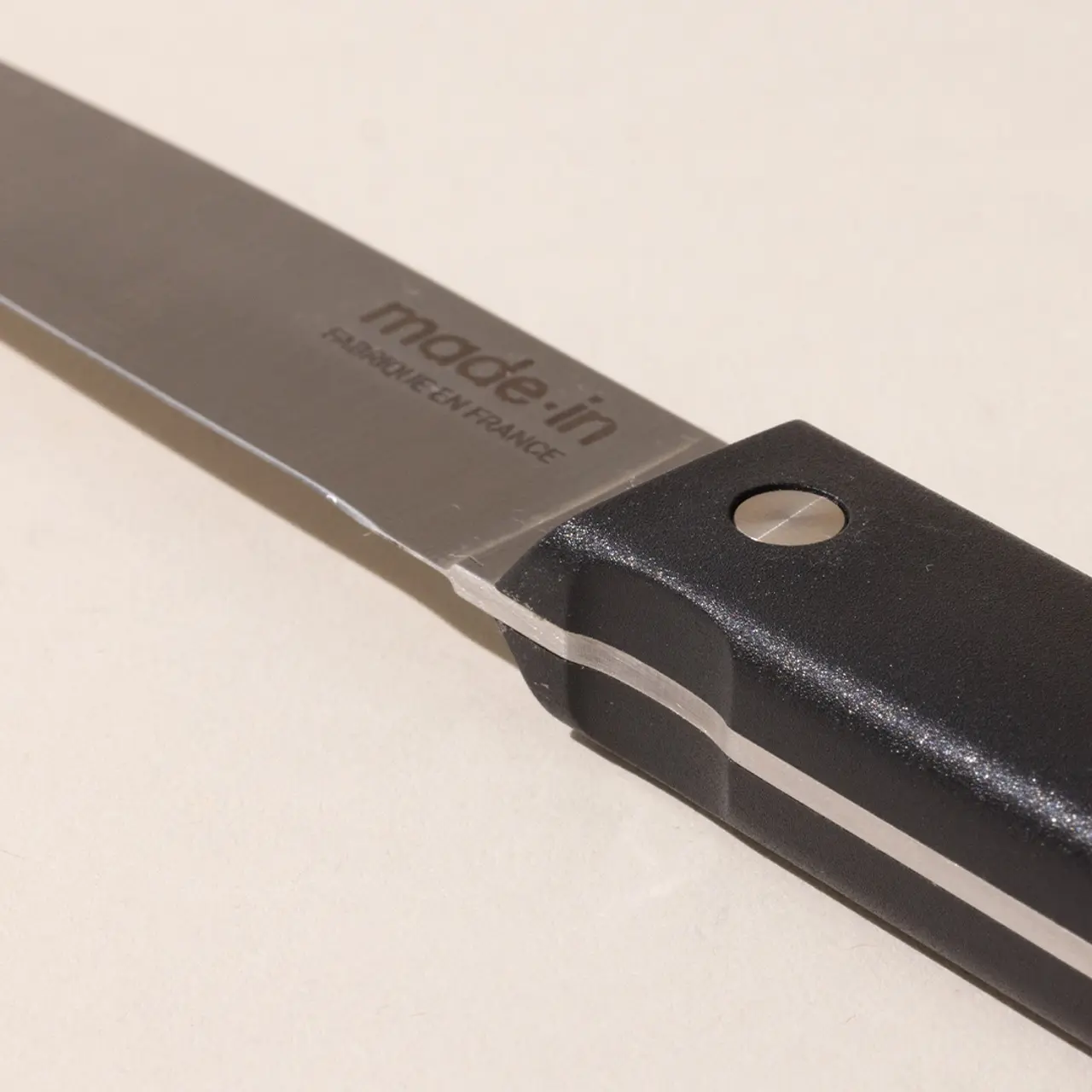 A close-up of a kitchen knife with the text "made in" on the blade and a black handle with a rivet.
