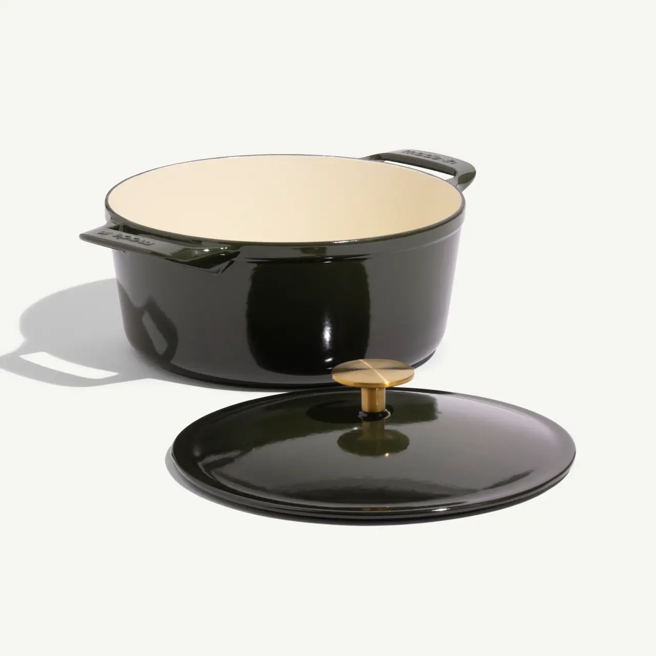 A dark green enamel pot with a lid and brass knob sits on a light background.