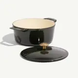 A dark green enamel pot with a lid and brass knob sits on a light background.