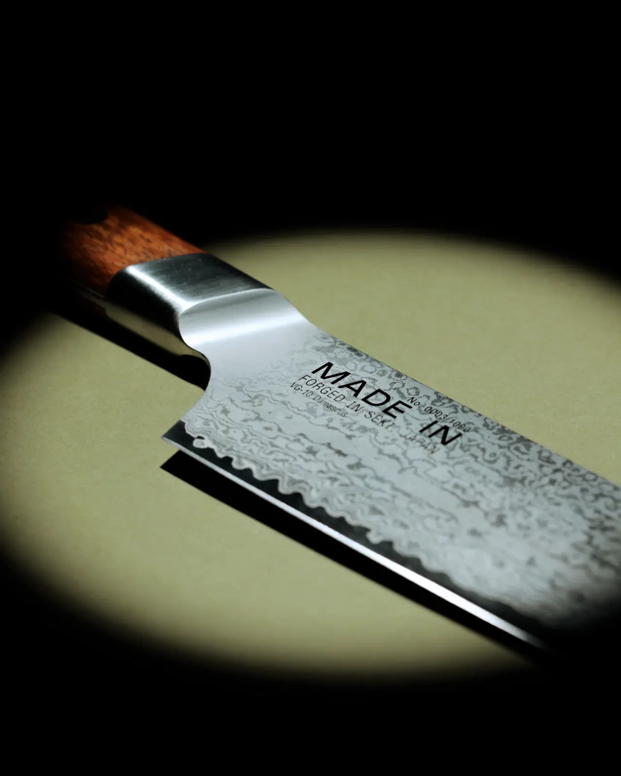 Close-up of a kitchen knife with a wooden handle and "MADE IN" text on the blade, spotlighted against a dark background.