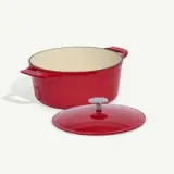 A red enameled cast-iron Dutch oven with its lid placed to the side on a white background.